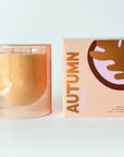 clear glass taupe candle next to packaging that says 'AUTUMN'