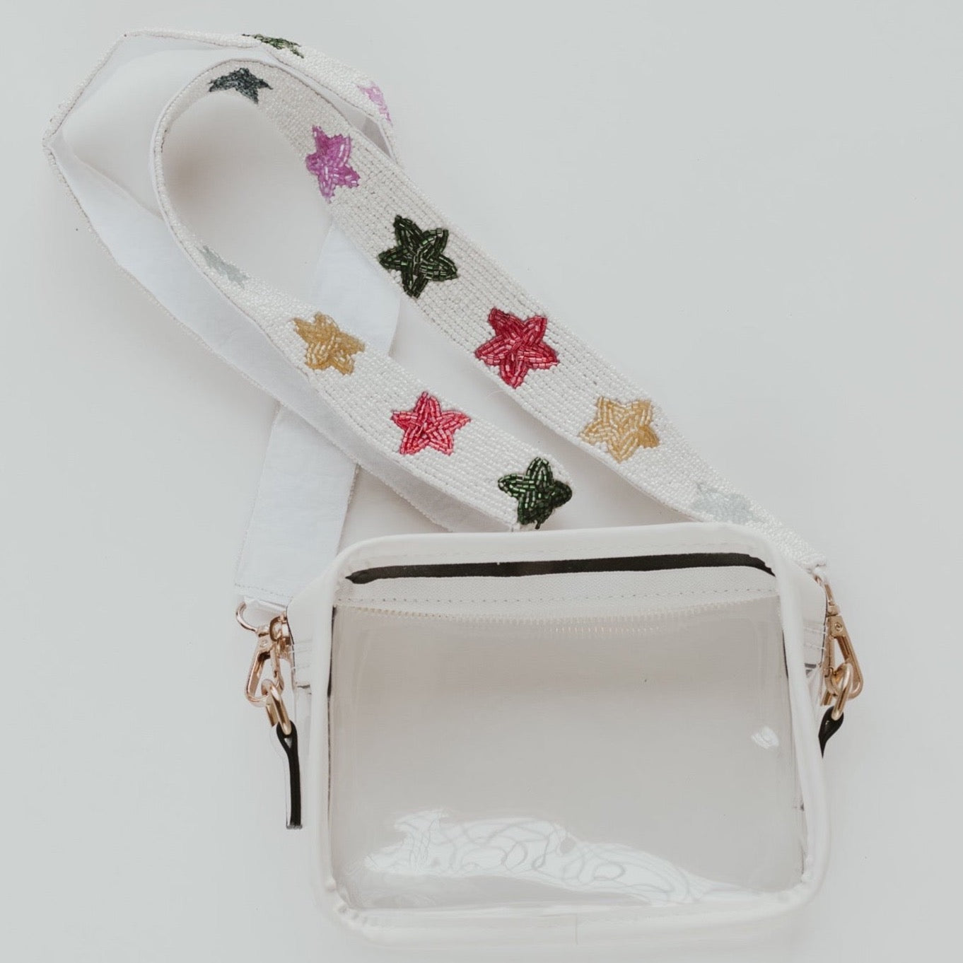 A clear purse with white lining and a white beaded bag strap with rainbow beaded stars along the length of the strap against a white background