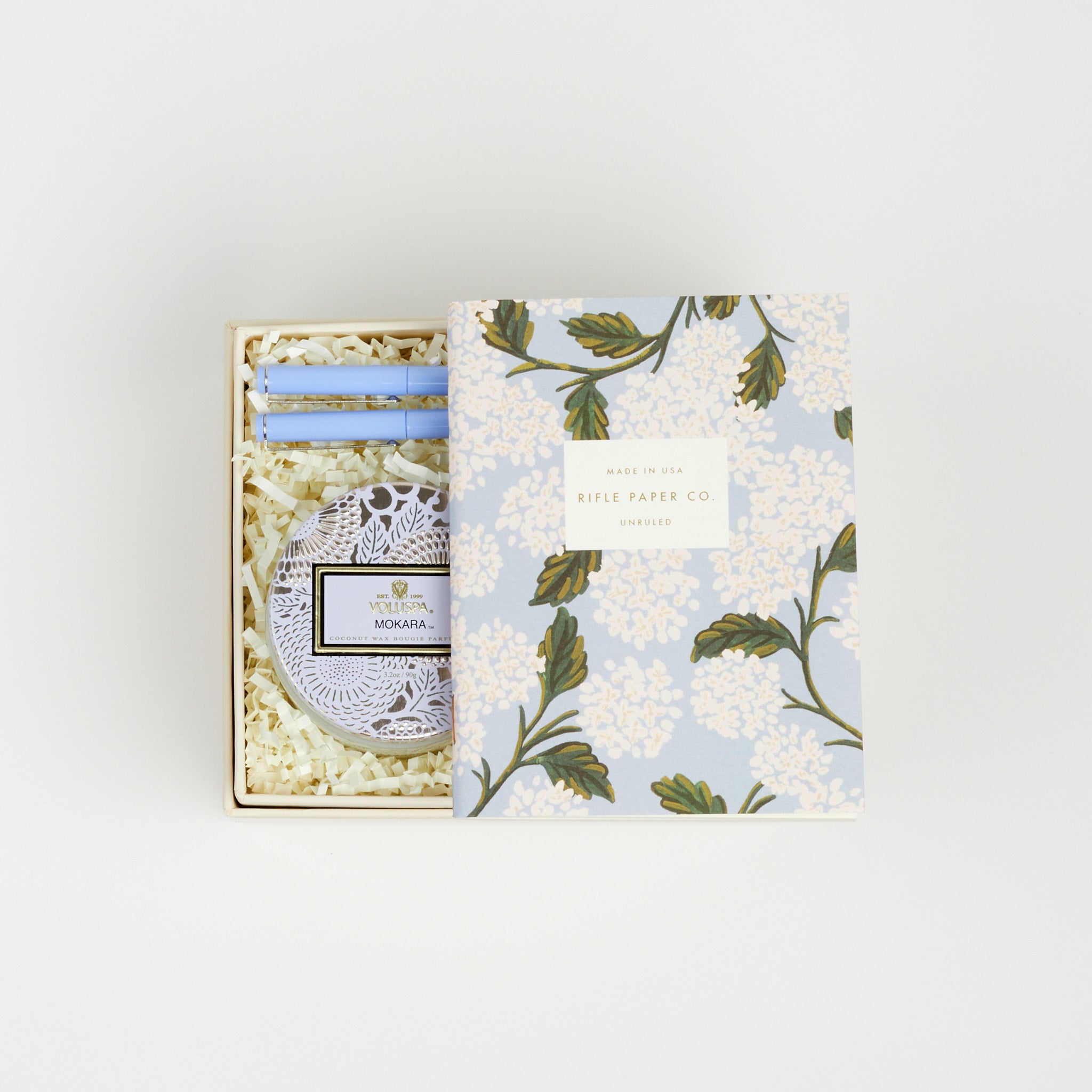 BOXFOX Original Creme Gift Box containing Rifle Paper Hydrangea Pocket Notebooks, 2 Periwinkle Le Pens, and Voluspa Mokara Petite Glass Jar Candle.