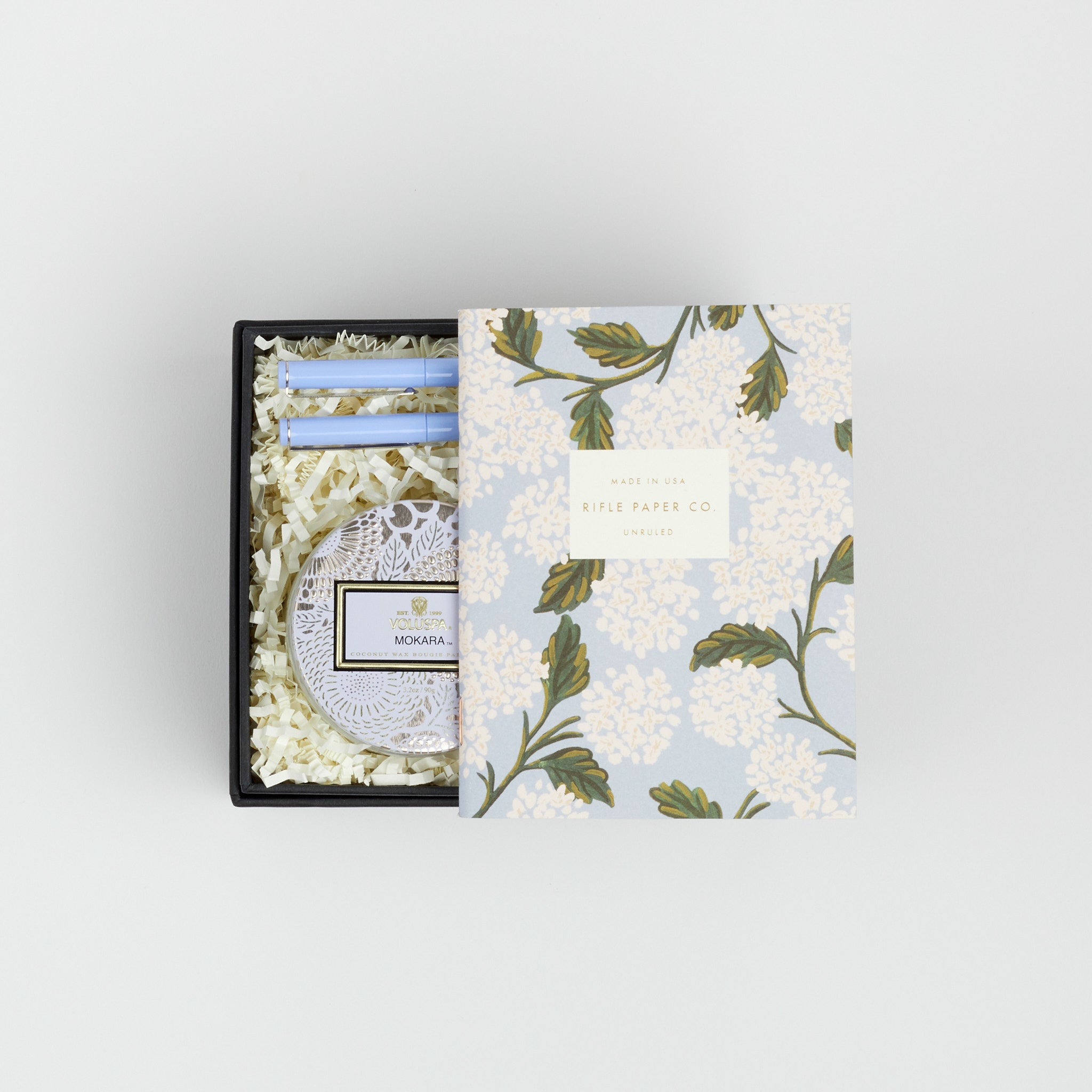 BOXFOX black Gift Box containing Rifle Paper Hydrangea Pocket Notebooks, 2 Periwinkle Le Pens, and Voluspa Mokara Petite Glass Jar Candle.