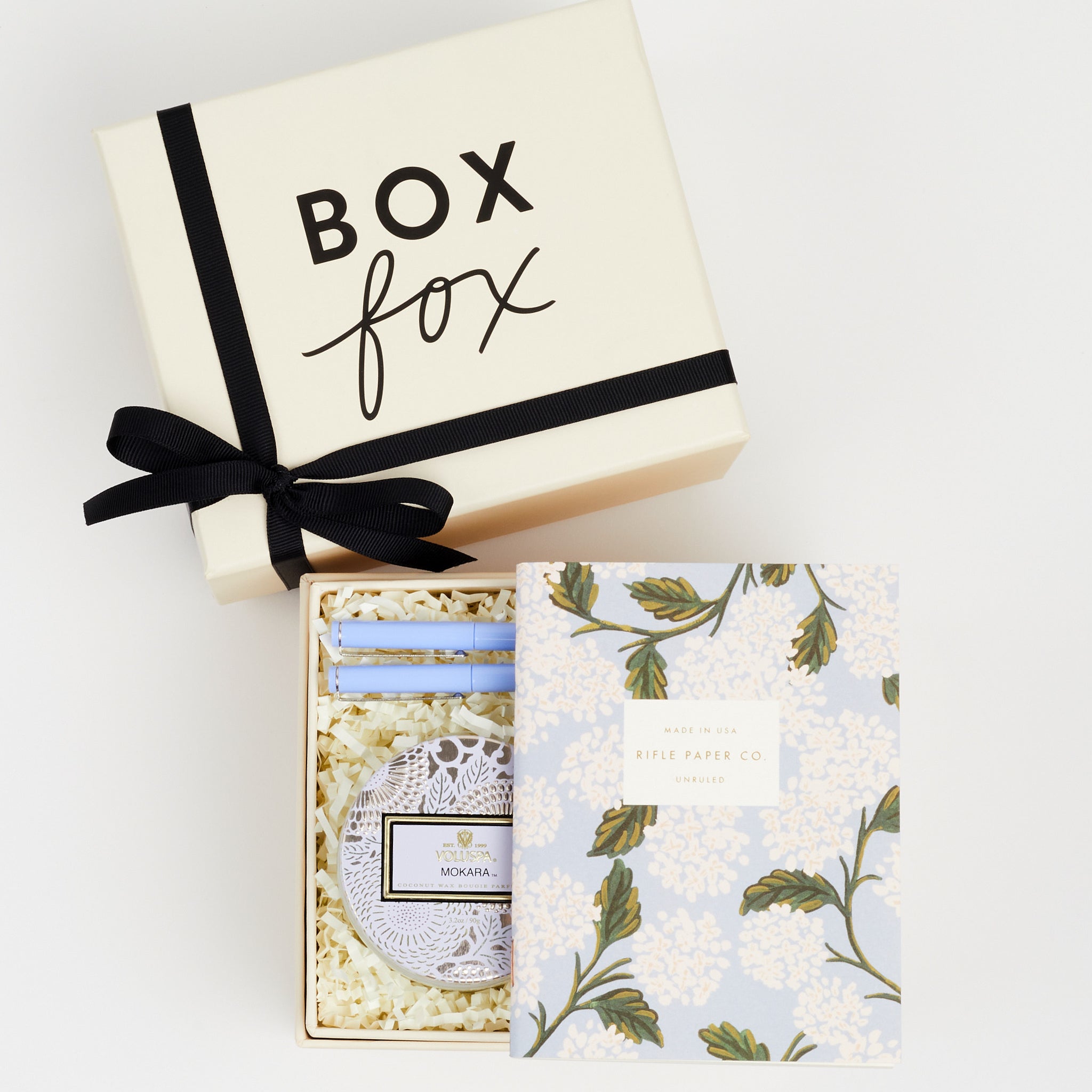 BOXFOX Original Creme Gift Box containing Rifle Paper Hydrangea Pocket Notebooks, 2 Periwinkle Le Pens, and Voluspa Mokara Petite Glass Jar Candle.
