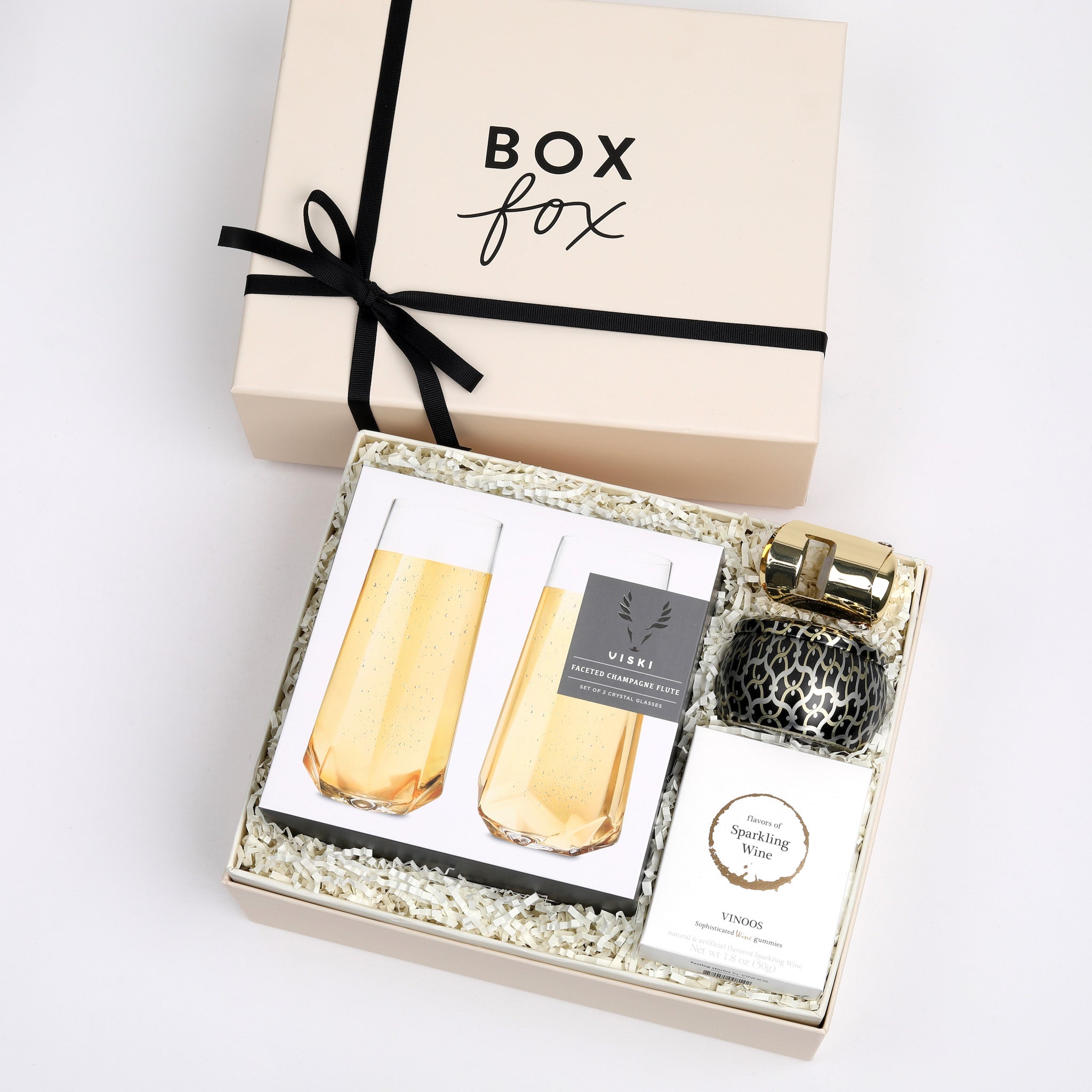 BOXFOX Original creme Pop Fizz Clink Gift Box packed with Voluspa Crisp Champagne Candle, Vinoos Champagne Gummies, Viski Gold Champagne Stopper, and Viski Pair of Champagne Flutes.