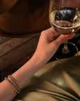 gold beaded bracelet set on wrist holding a glass of wine