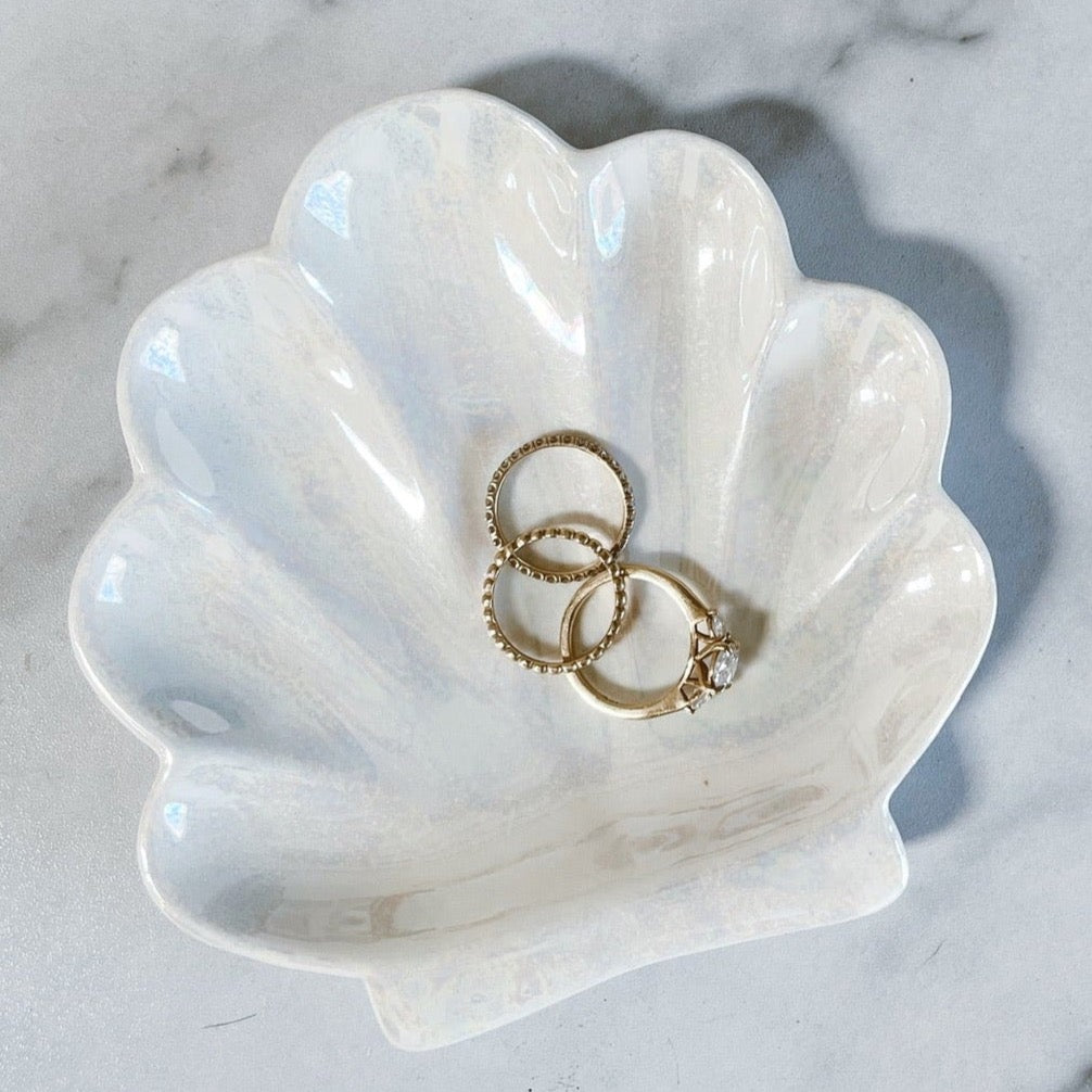 Ceramic seashell trinket tray holding 3 gold rings against a white marbled background
